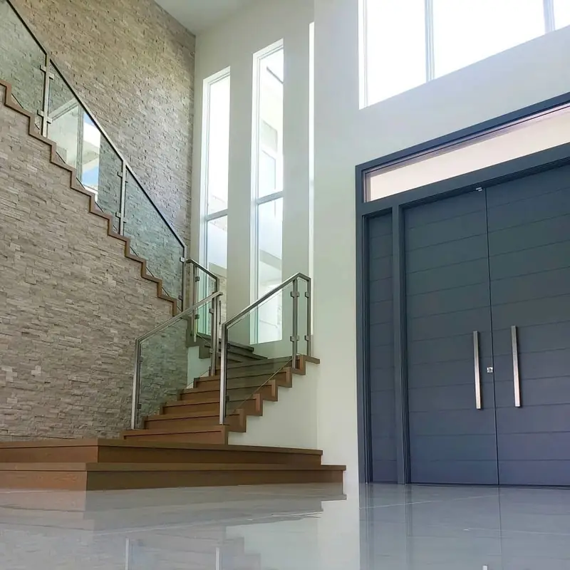 A stone-clad stairwell with a glass and steel railing beside dark modern entry doors, finished by Creative Images Painting