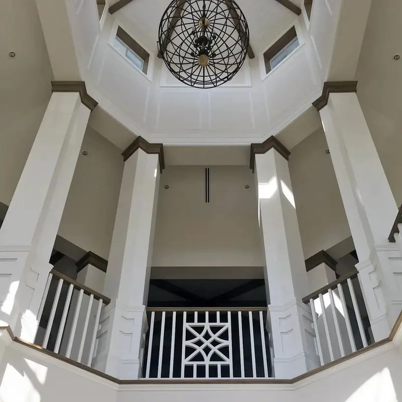A soaring octagonal foyer with a wood-beamed ceiling, wrought-iron chandelier and crisp white millwork