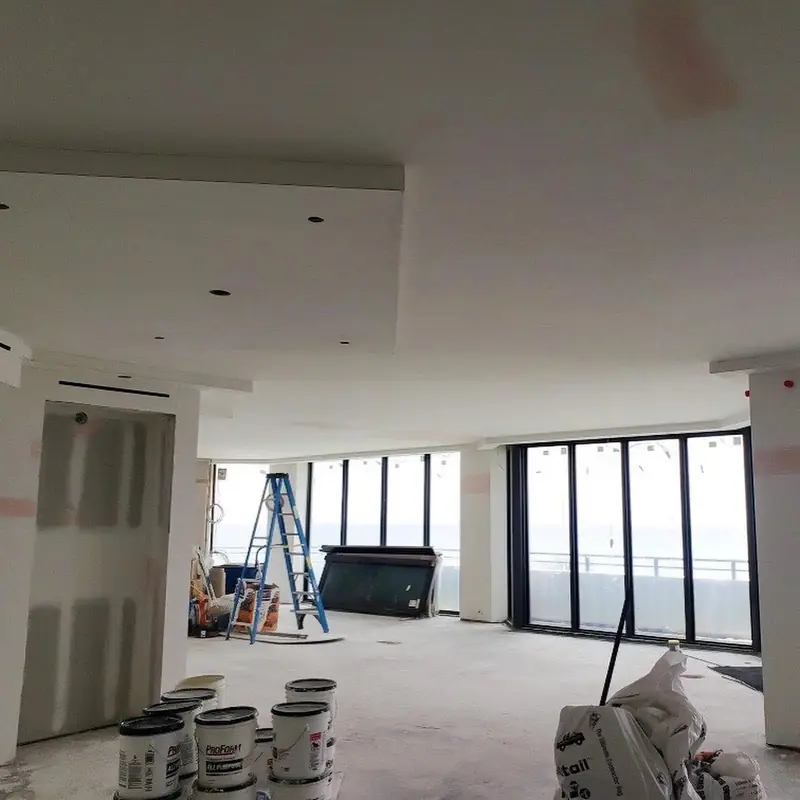 An oceanfront interior mid-job with ladders and paint buckets, protected before work begins