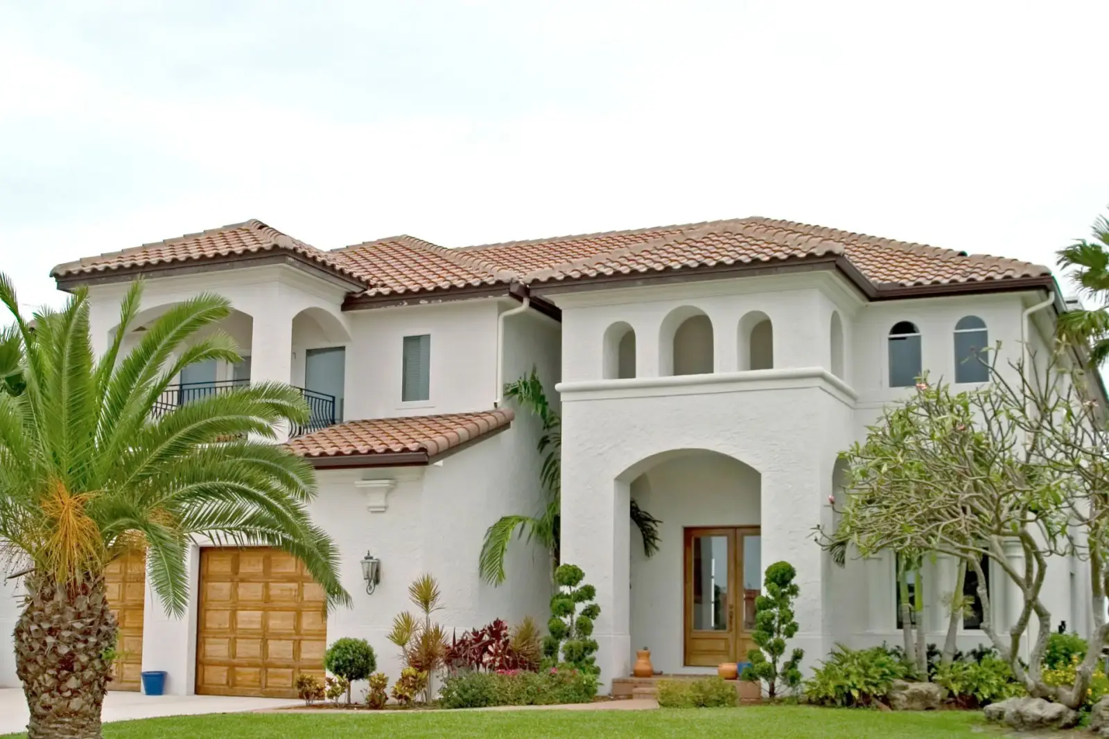 A Mediterranean style two-storey estate in freshly painted white stucco with a terracotta tile roof and wood double entry doors